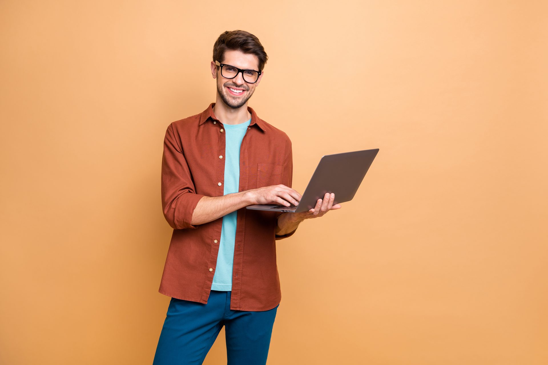 Smiling man holding a laptop against an orange background